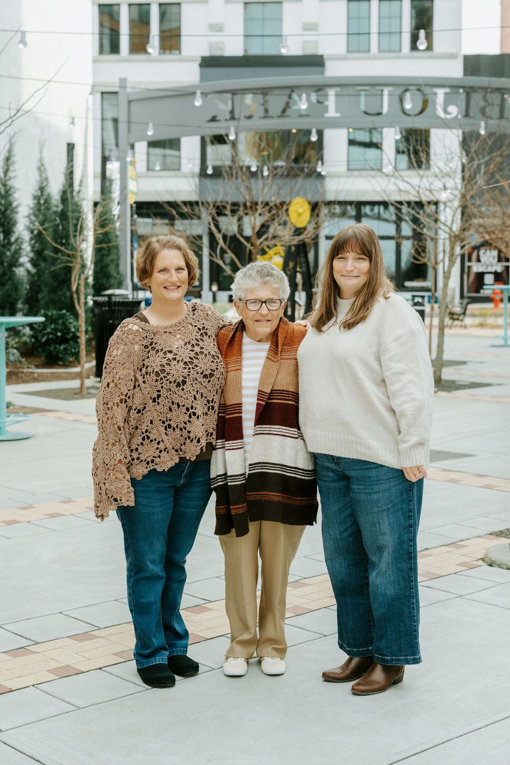 Three people standing together on a city sidewalk wearing casual winter clothing.