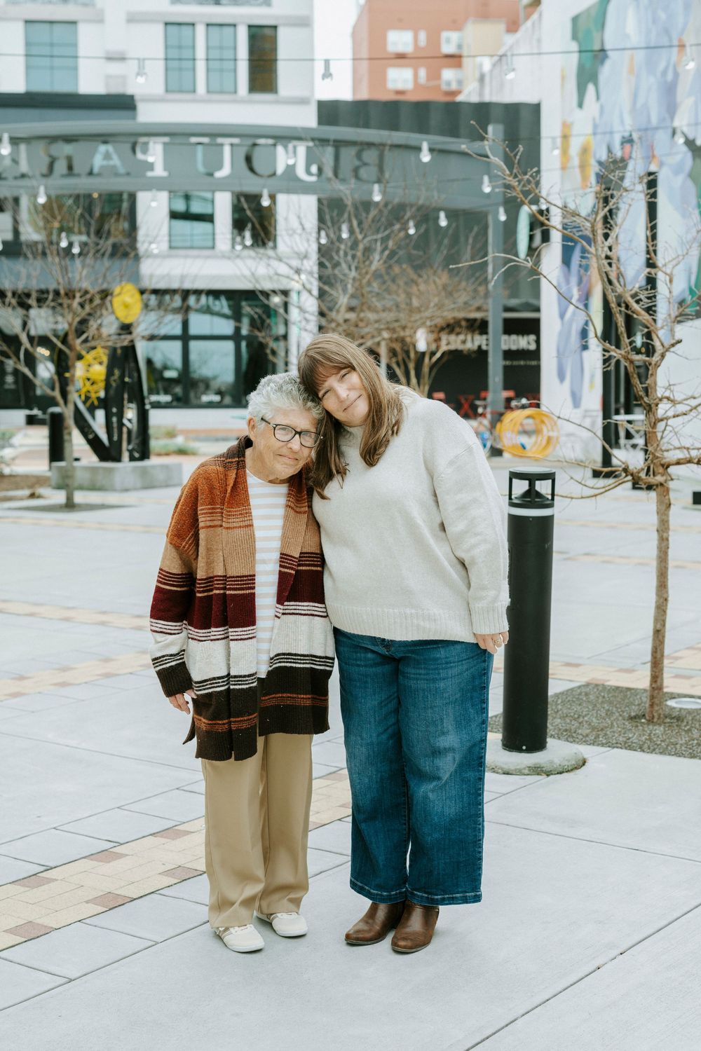 Two people in casual winter outfits share a sweet moment together on an urban sidewalk during a cold day.