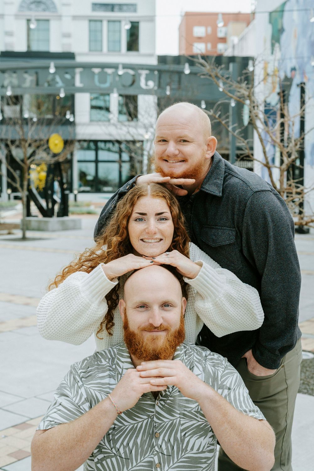 Three friends pose playfully together on a city street, stacking their heads in a creative portrait.