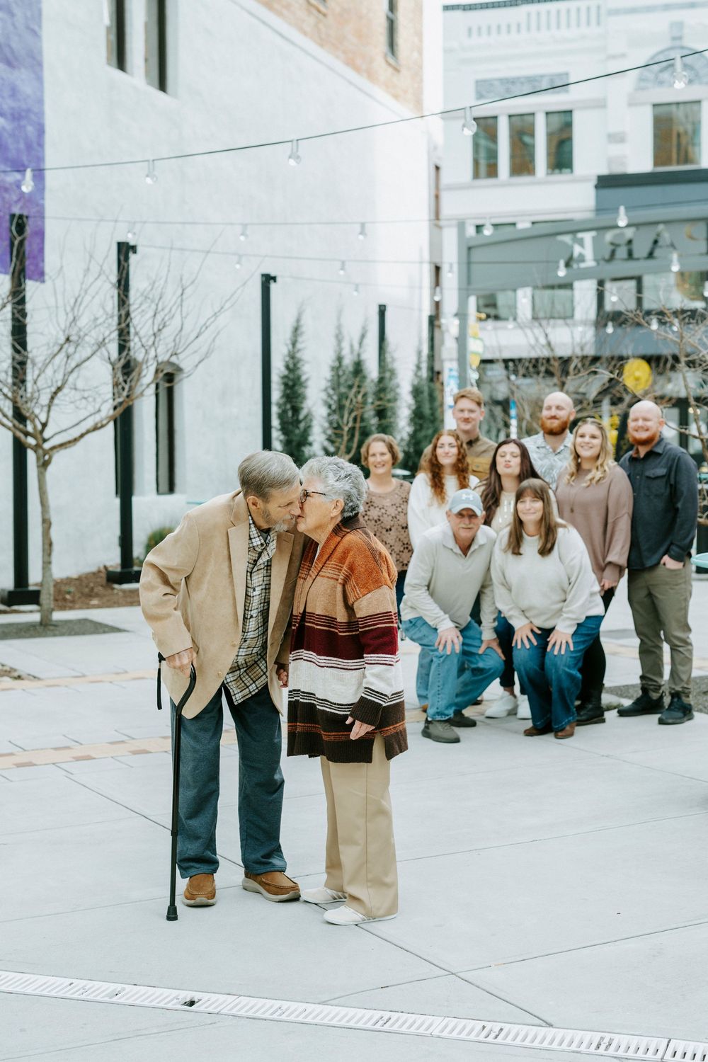 A group of people in coordinated winter outfits pose together on a city sidewalk near modern buildings.