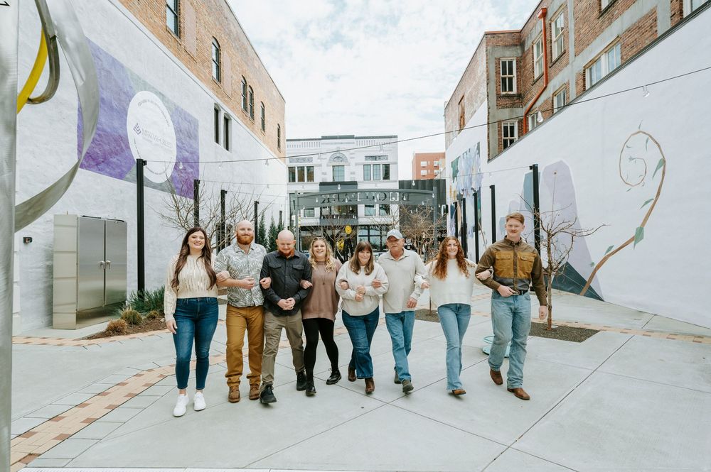 A group of friends walk together down an urban alleyway decorated with wall murals on a sunny day.