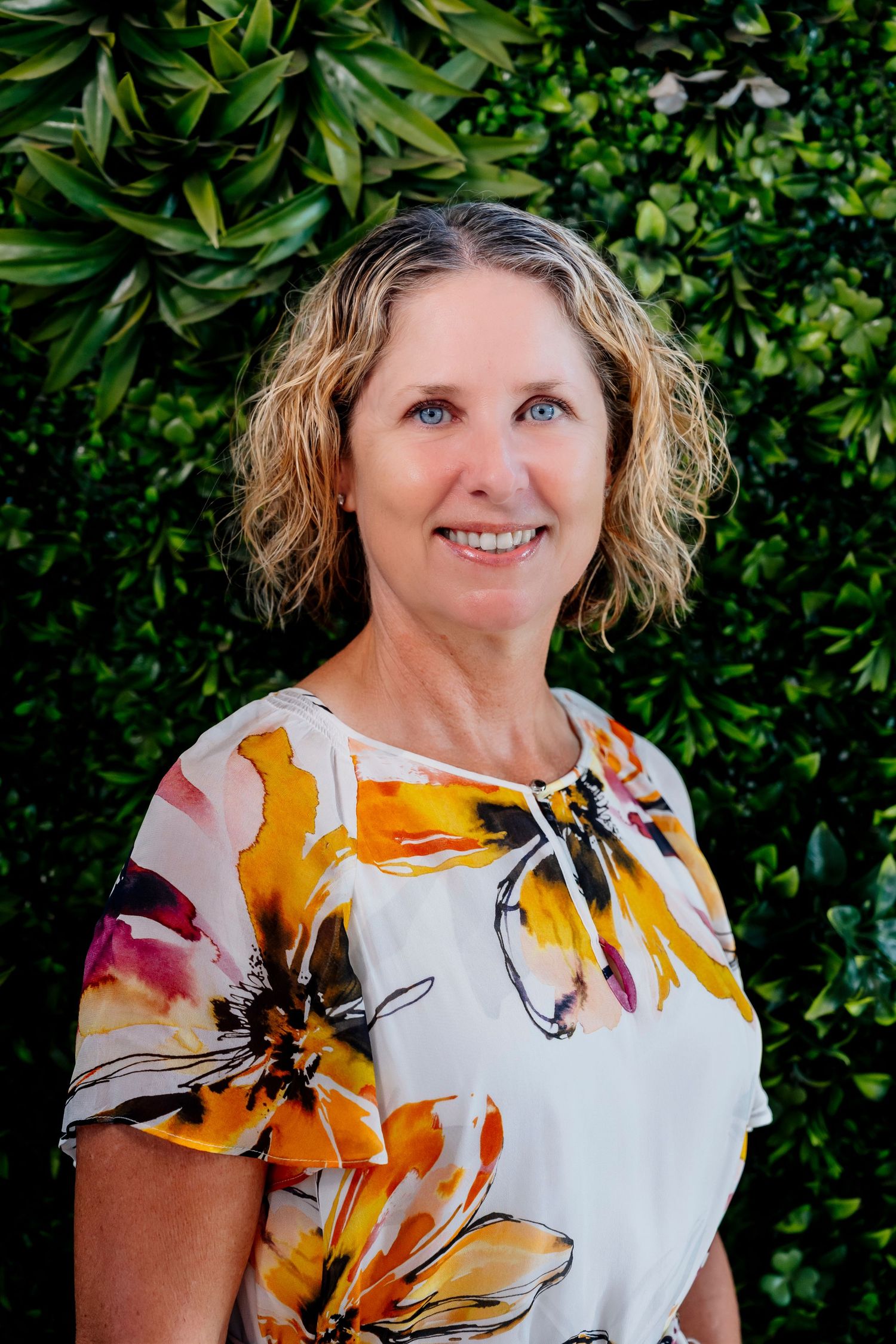 A close-up photo series showing someone wearing a white blouse with vibrant yellow and orange floral patterns against green foliage.