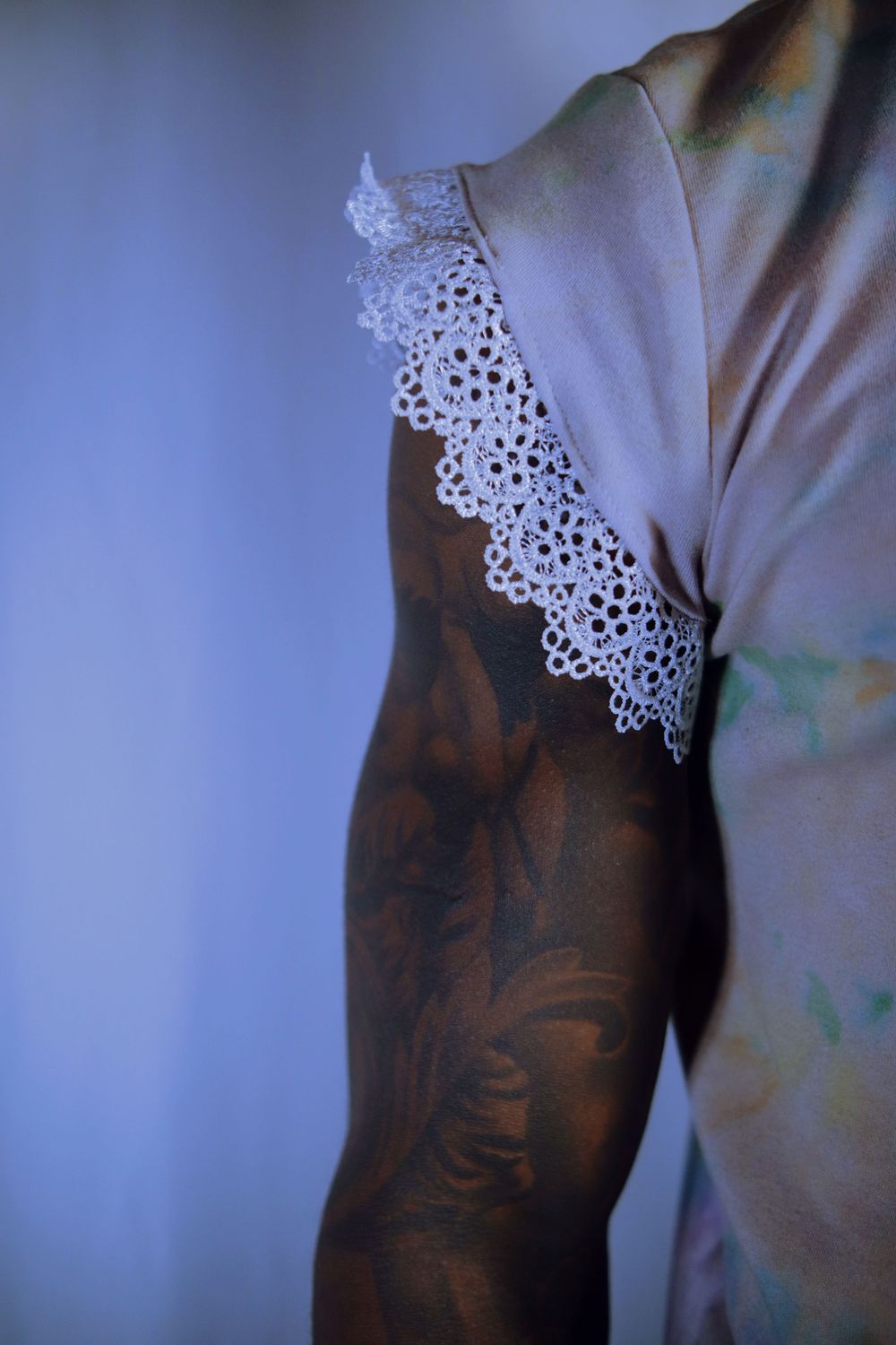Delicate white lace trim detail on a light colored garment against a shadowy blue background.
