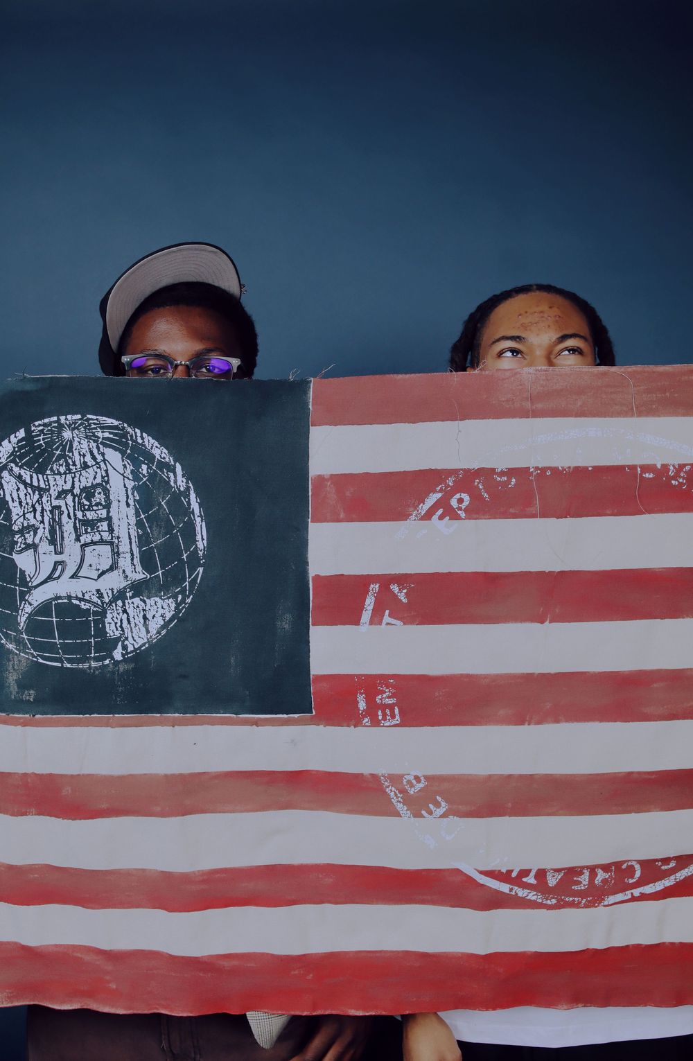 People peek through gaps in a segmented American flag display creating an artistic composition.