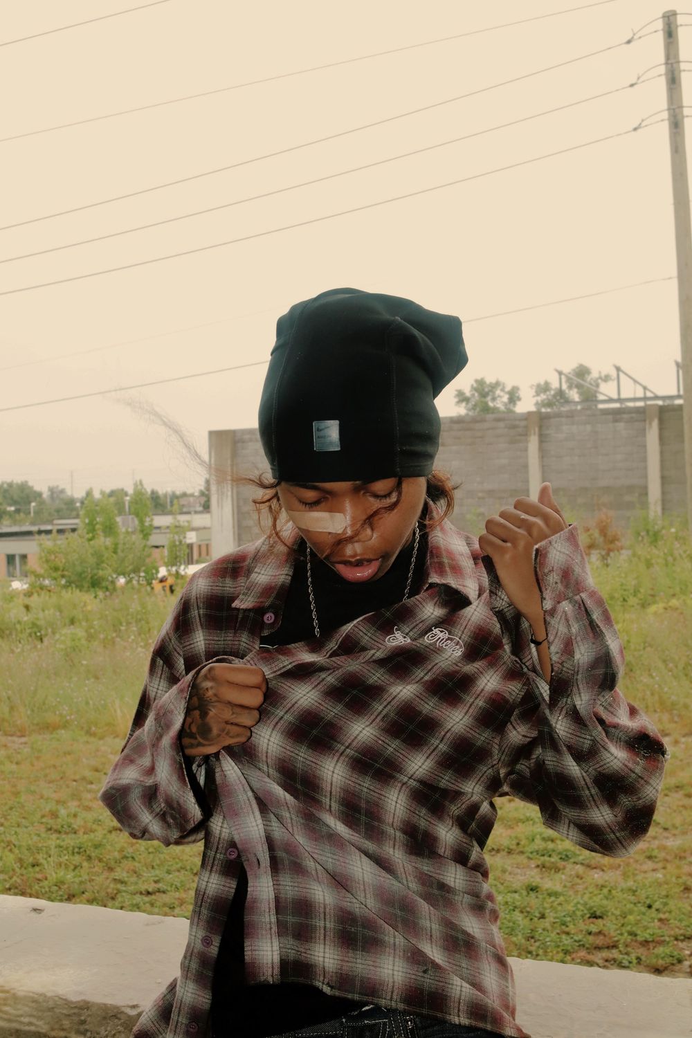A sequence of images showing someone in a plaid shirt and cap performing a sneezing action outdoors.