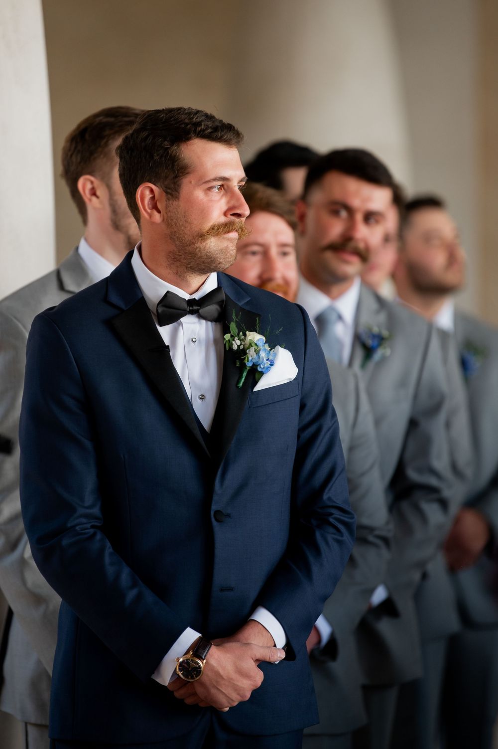 Groomsmen in navy and gray suits lined up at formal wedding ceremony.