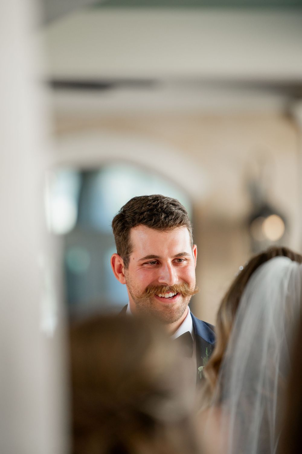 Wedding ceremony moment captured through white columns in elegant venue.