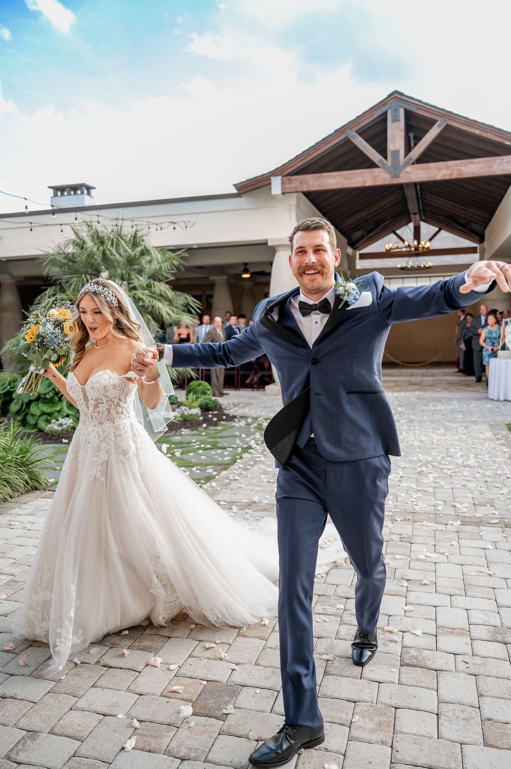 A couple in wedding attire dances playfully on an outdoor stone patio.