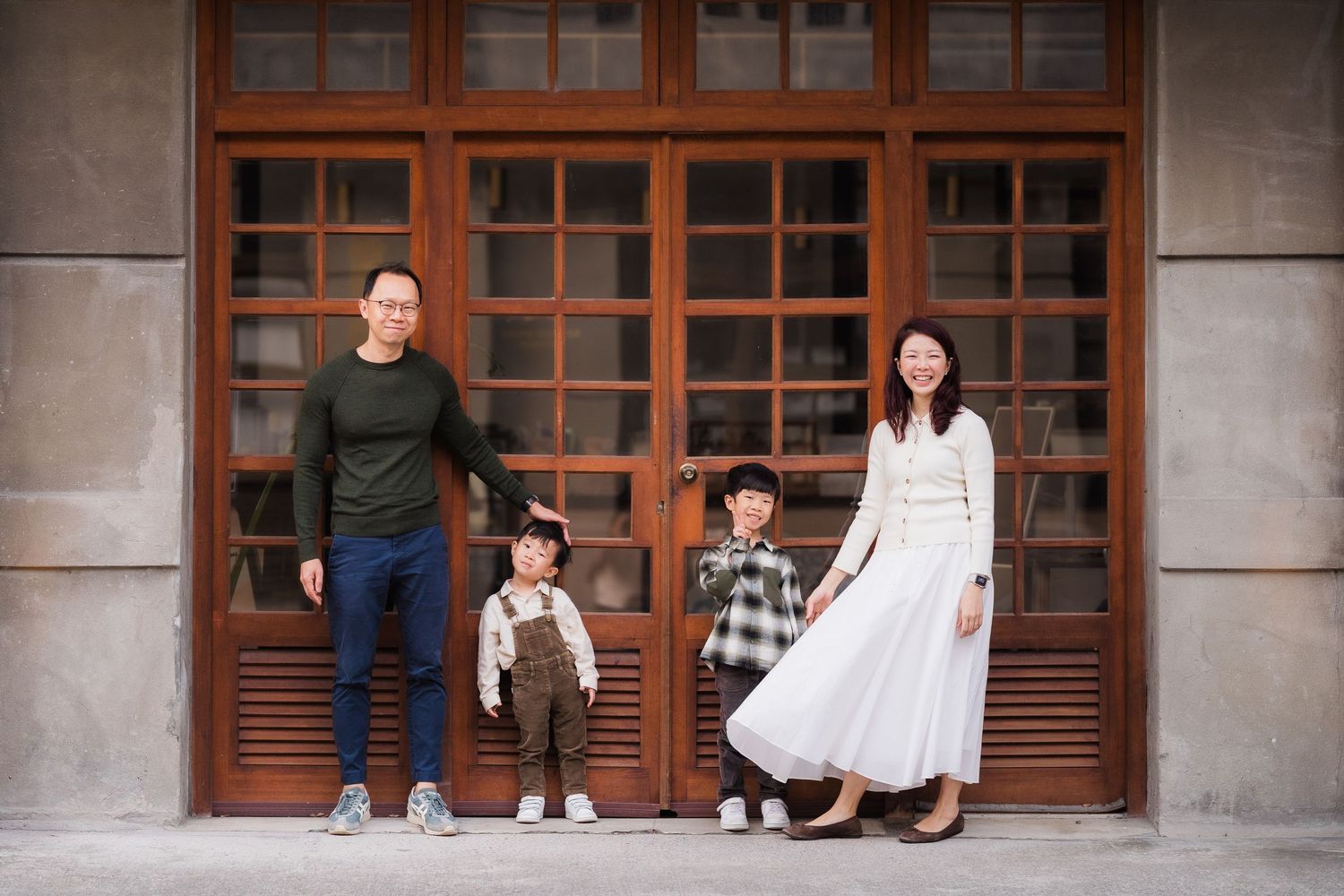 A family stands together in front of wooden doors of a building, wearing casual and dressy attire.