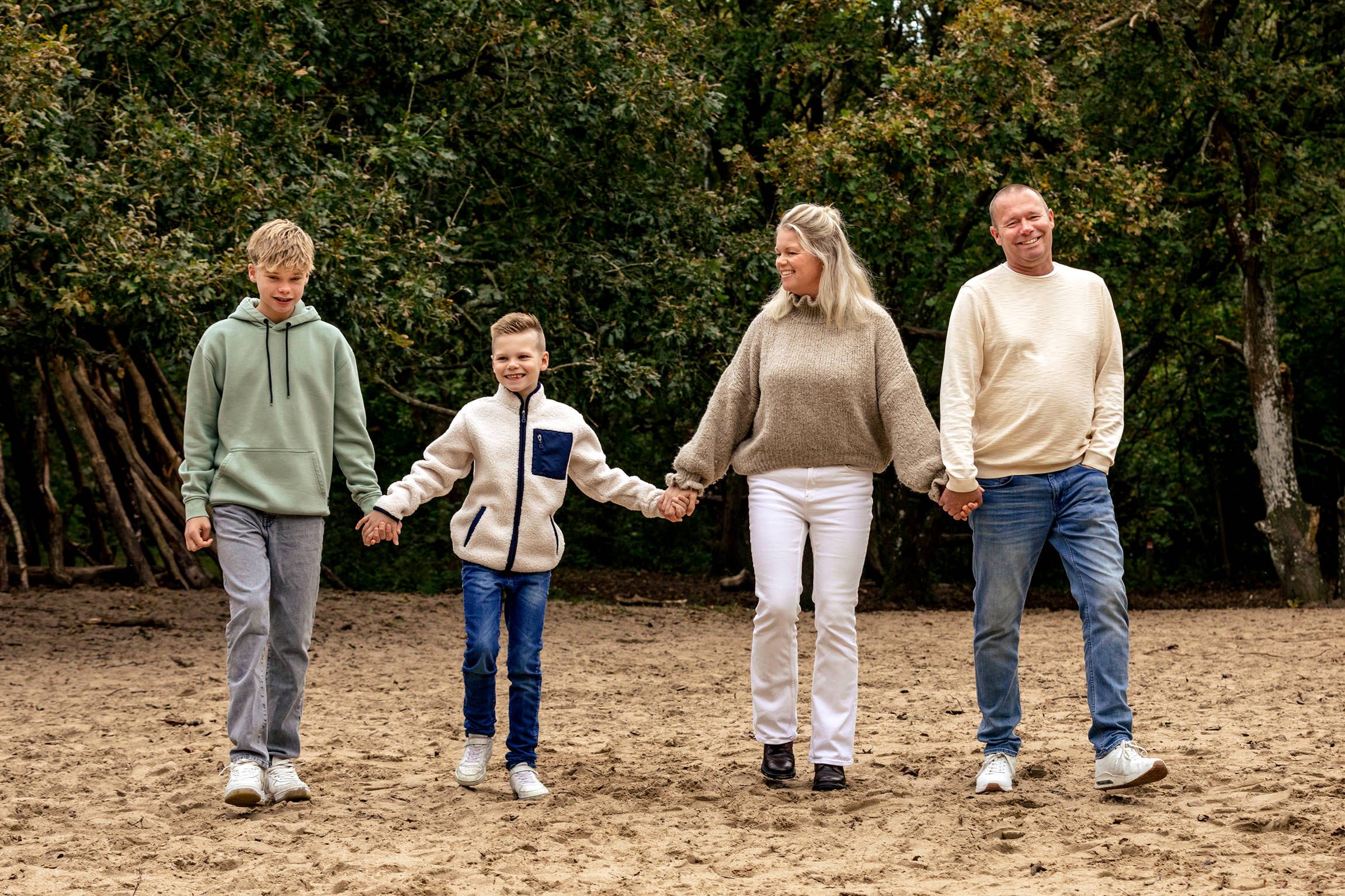 Gezin met vader, moeder, tiener en jonger kind loopt hand in hand door het bos in Castricum tijdens een gezinsfotoshoot, vastgelegd door Luz