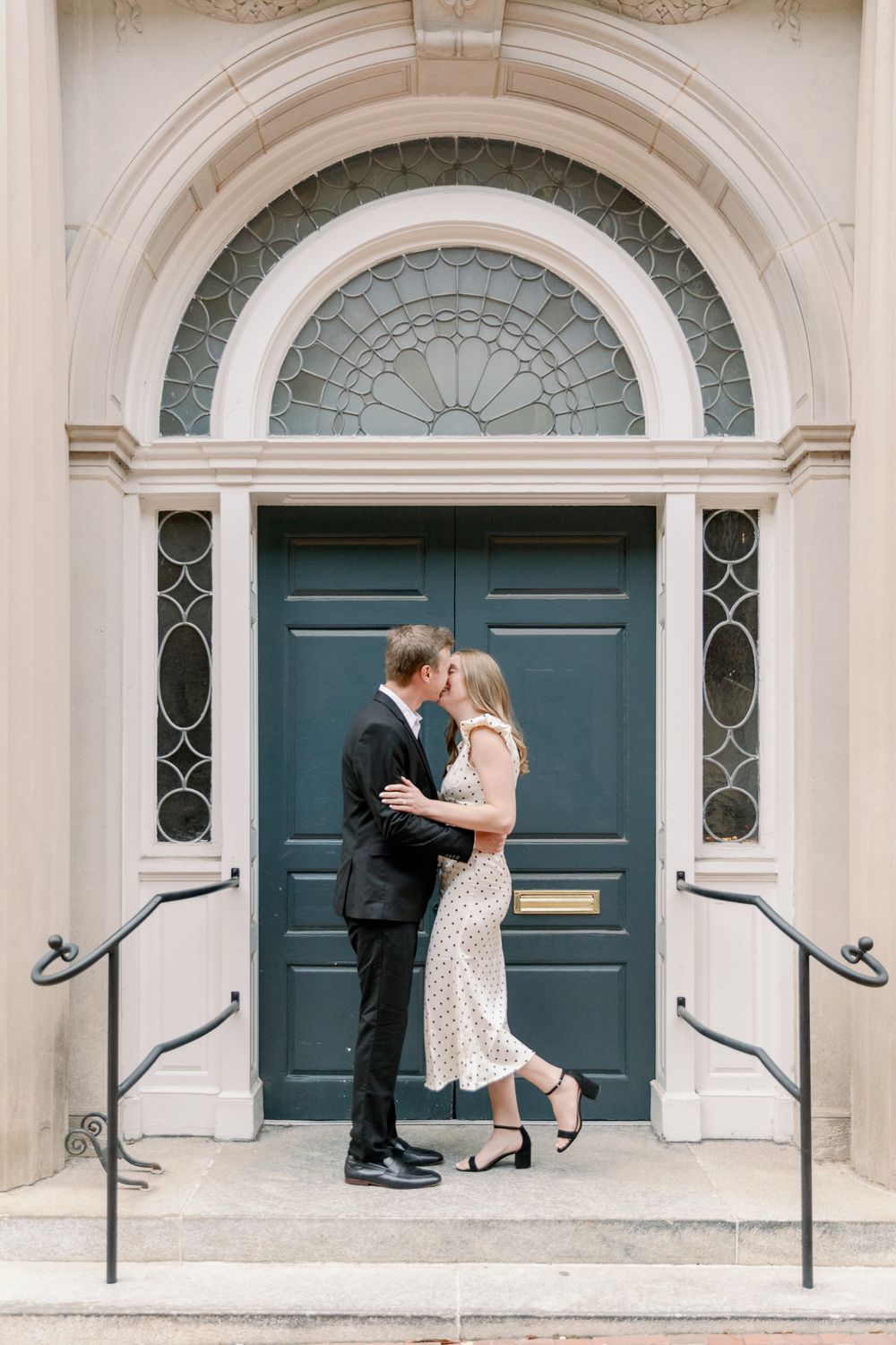 Romantic couple embraces in front of elegant arched doorways with blue doors and ornate architectural details.