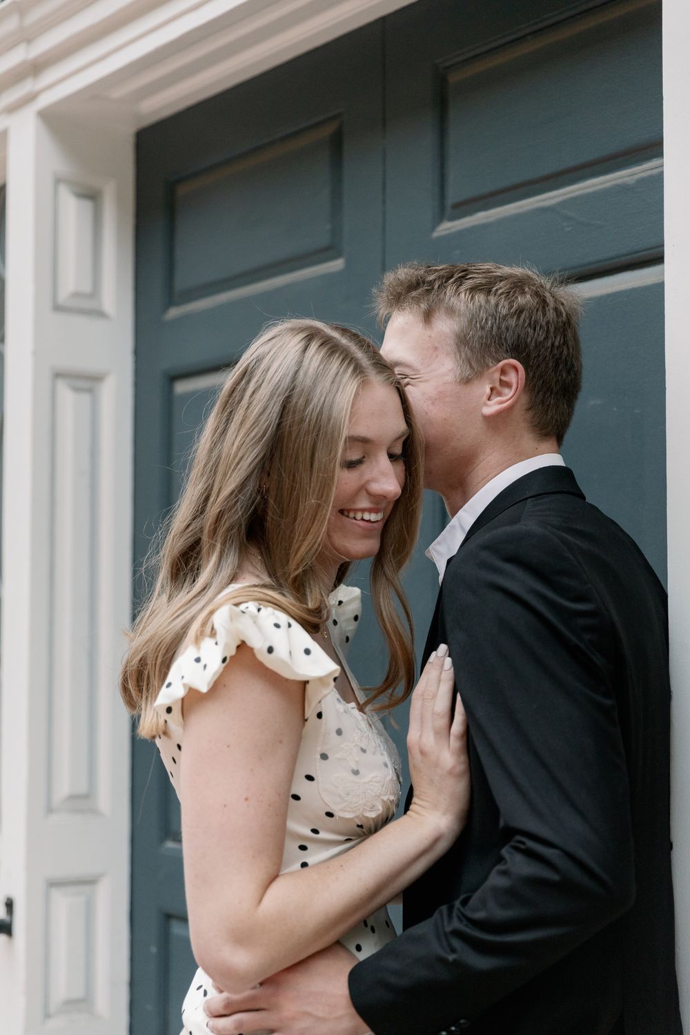 A romantic couple sharing an intimate moment in front of white columns wearing polka dot dress and suit.