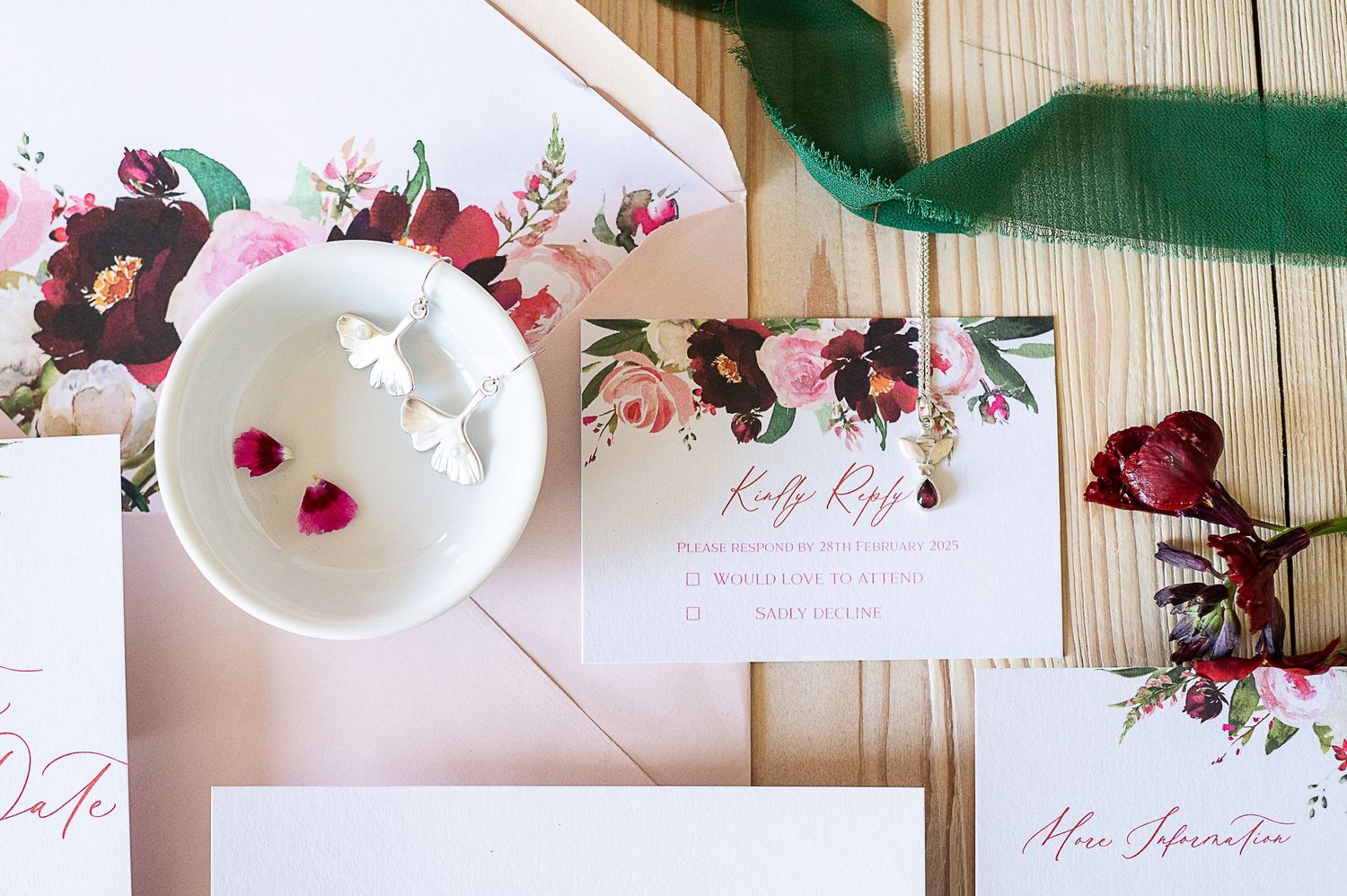 Wedding stationery and jewellery are laid out on a pale table...earrings are silver and the cards designed with green and pink florals