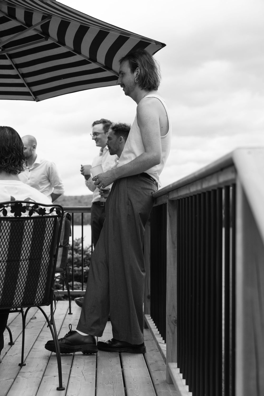 People gathered on a deck under a striped umbrella having conversations.