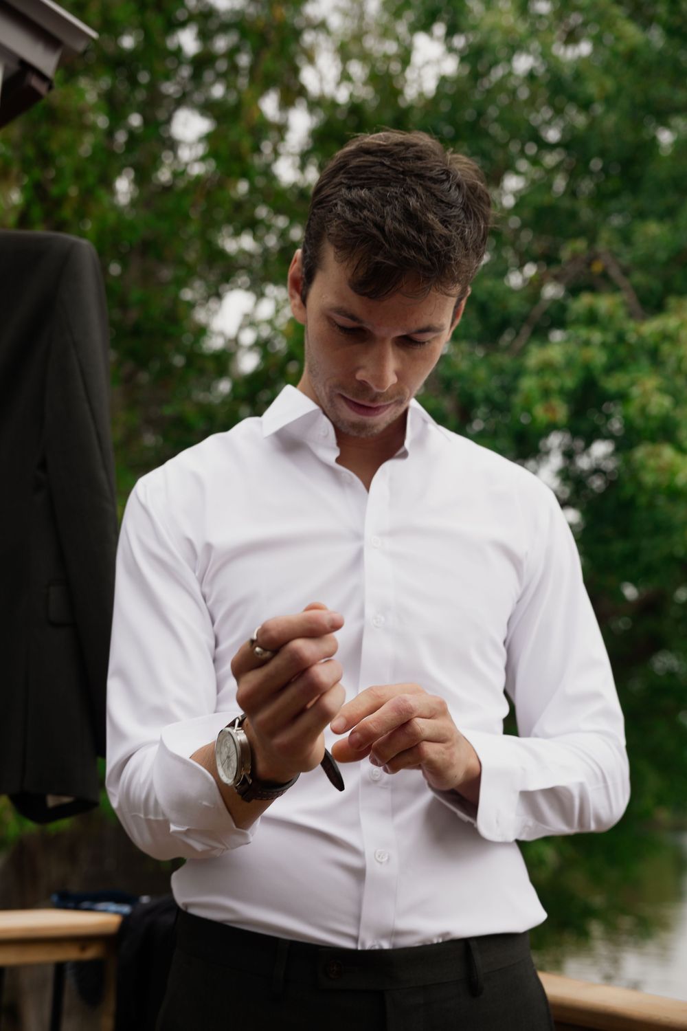 Person in white dress shirt adjusting cuffs while standing outdoors.