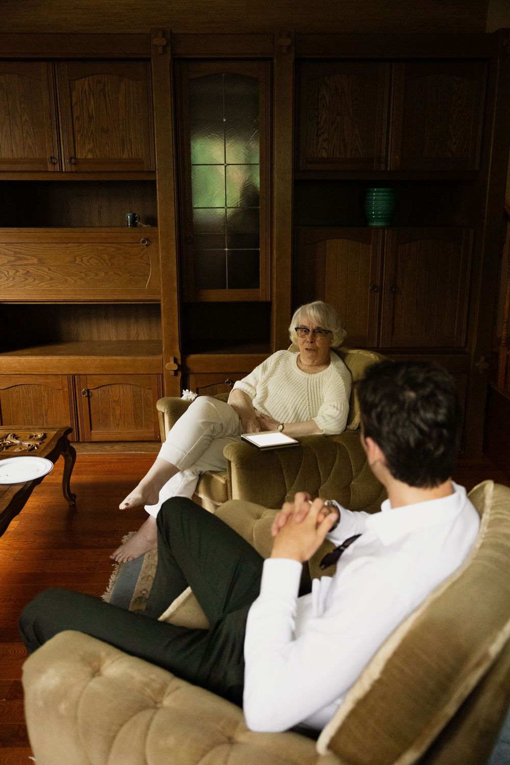 People relaxing on beige couches in a dimly lit room with wooden paneling.
