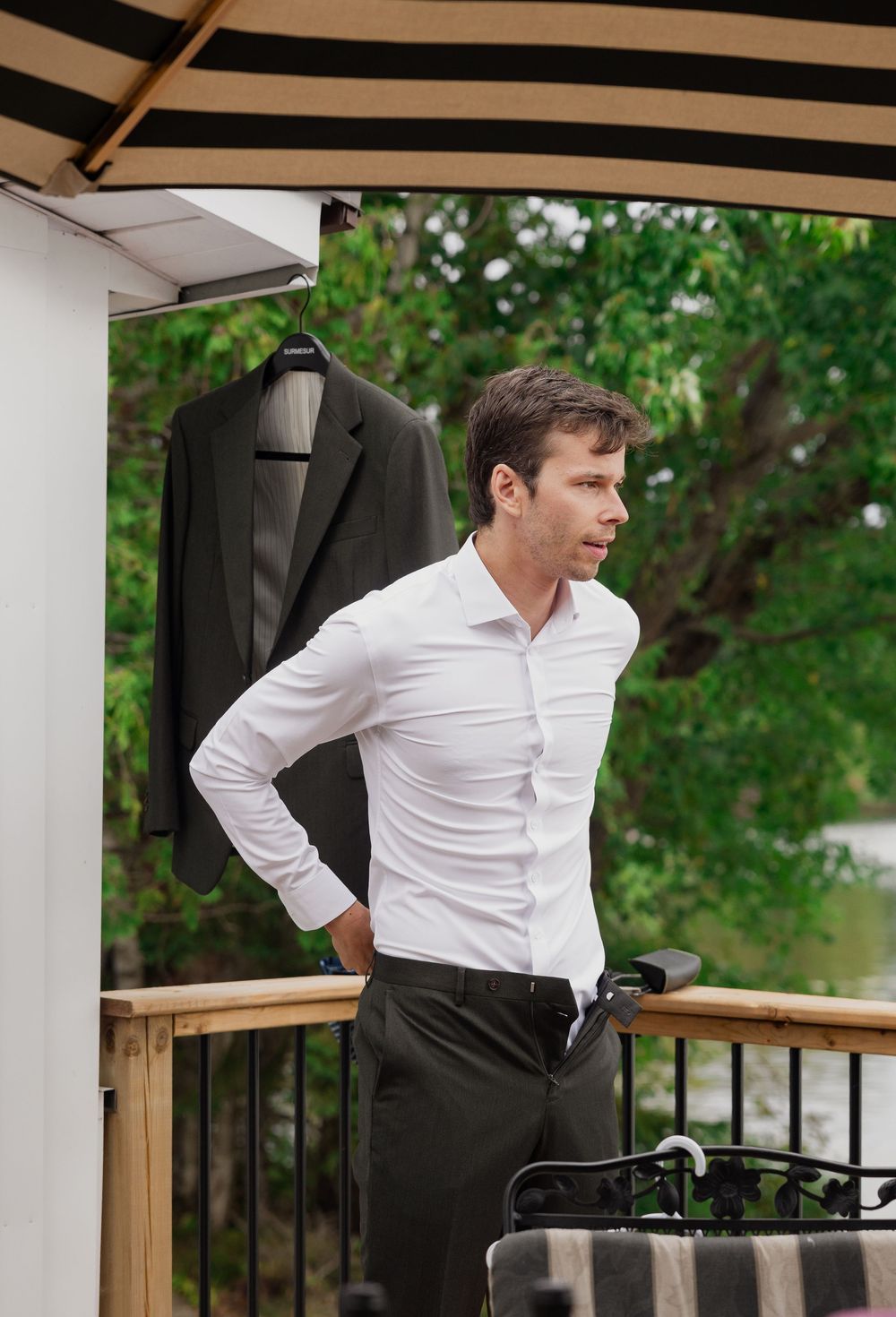 Person in white dress shirt and black pants standing on outdoor deck with striped umbrella.