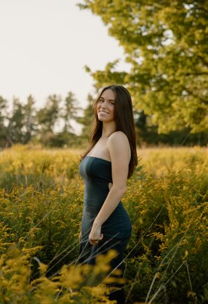 A person in a dark dress poses gracefully among yellow wildflowers at sunset.