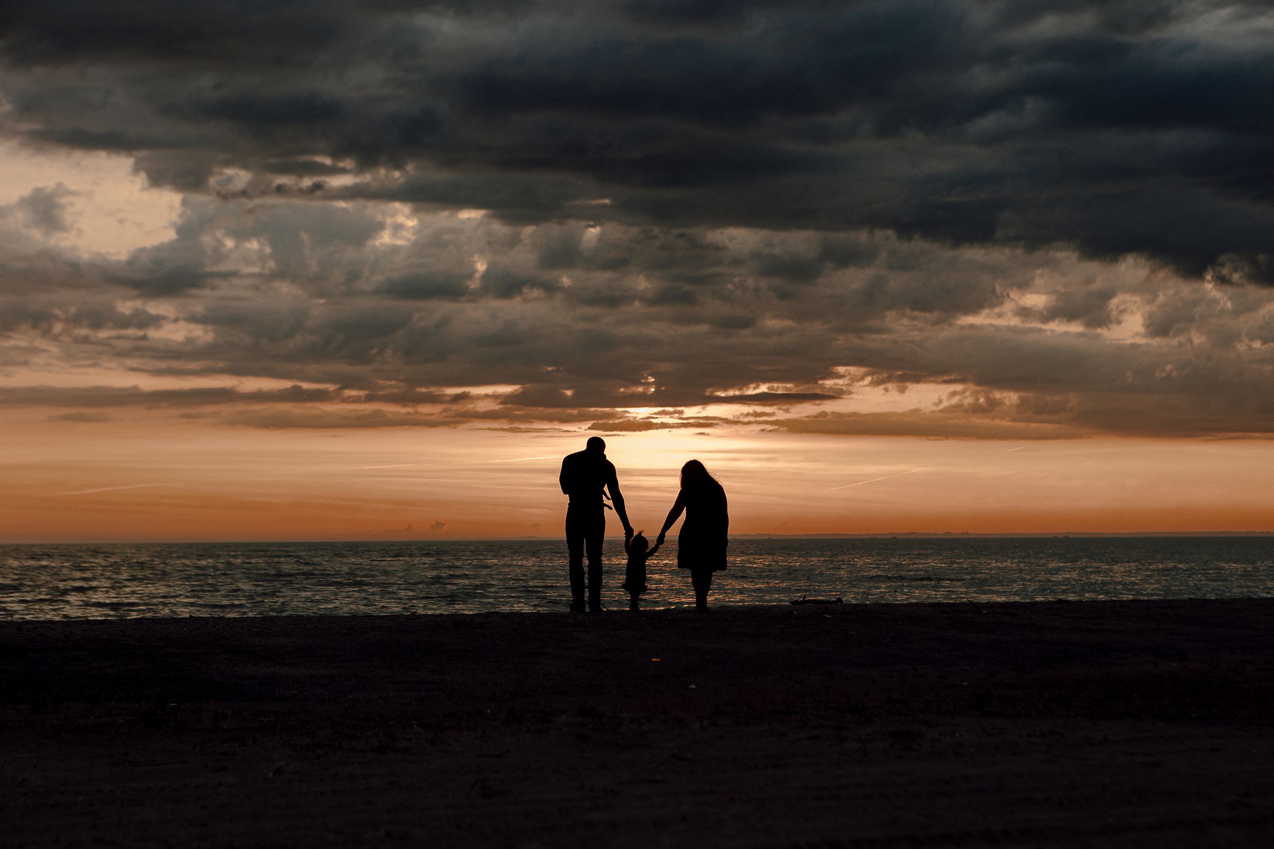Dramatic sunset silhouettes against stormy clouds over a dark landscape horizon.