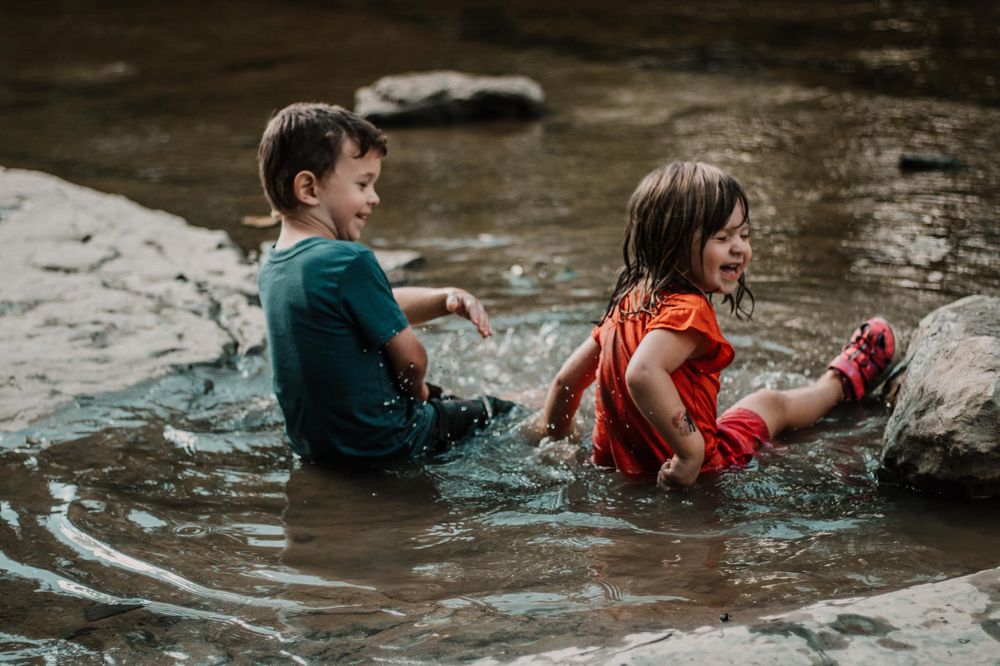Two people splash and play in a rocky stream during a summer adventure.