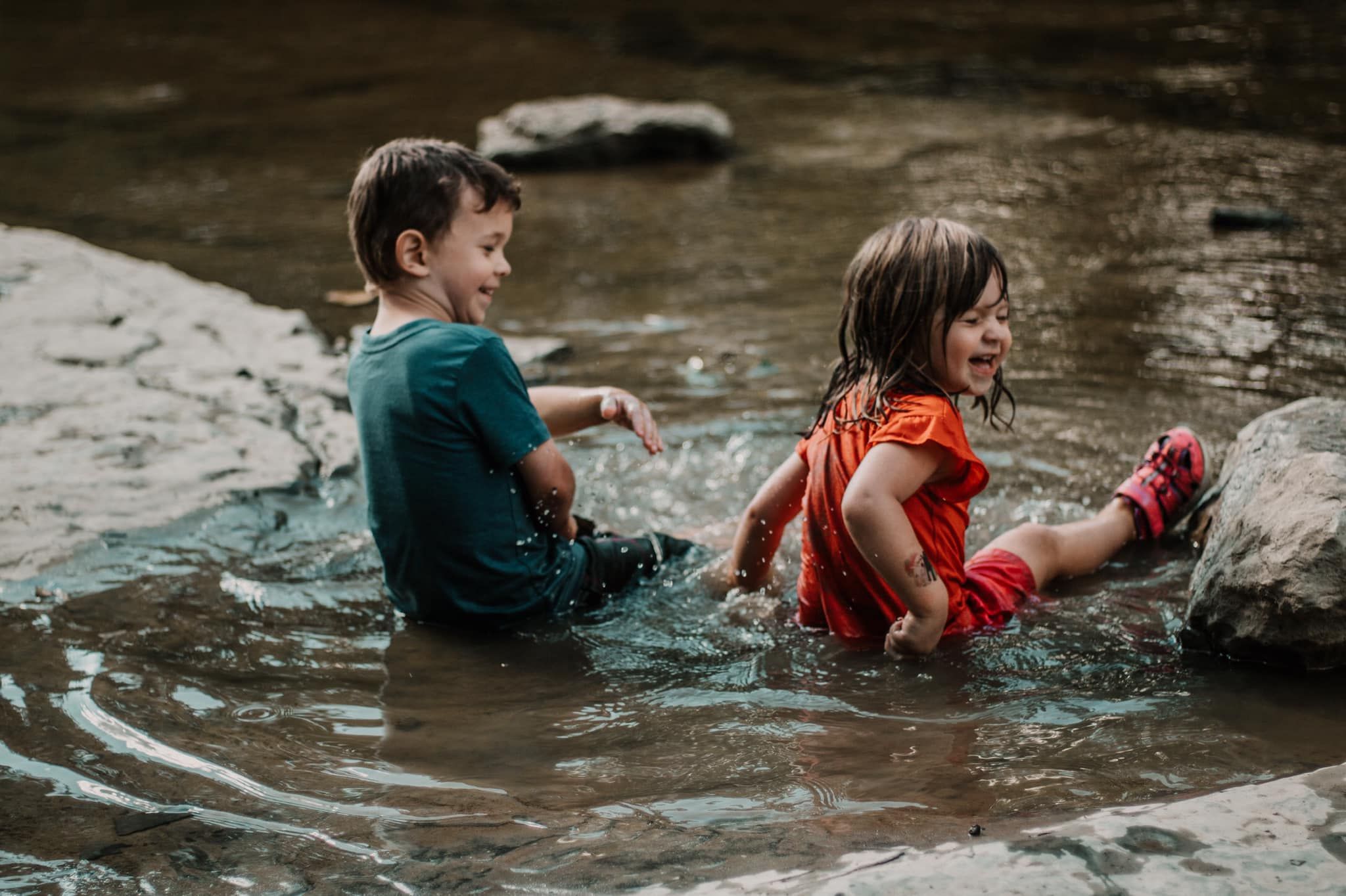 Two people splash and play in a rocky stream during a summer adventure.