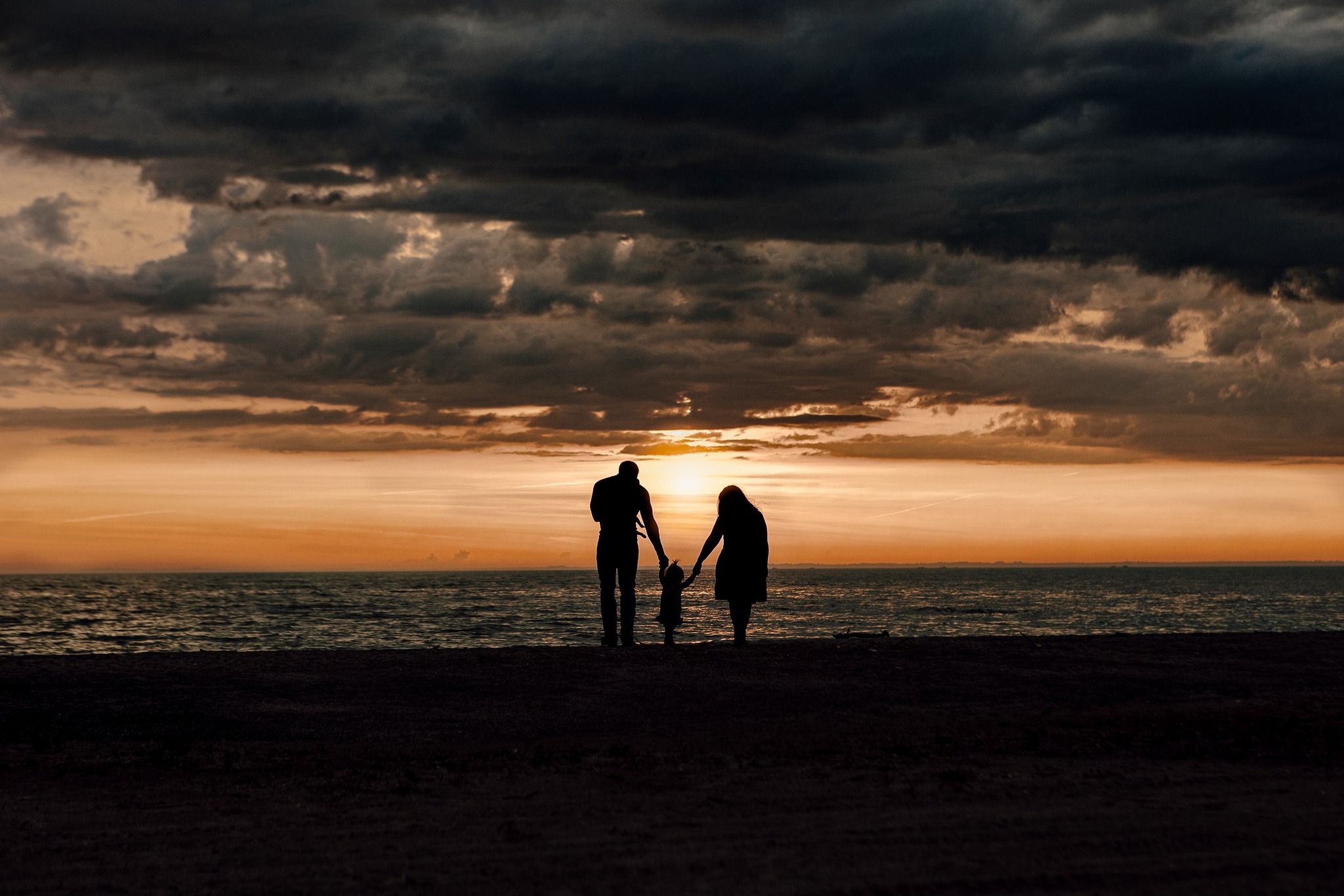 Two silhouettes stand against a dramatic sunset sky over the ocean.