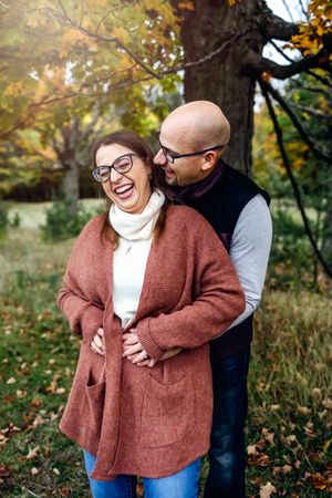 Playful autumn photoshoot showing joyful moments between two people in a park setting.