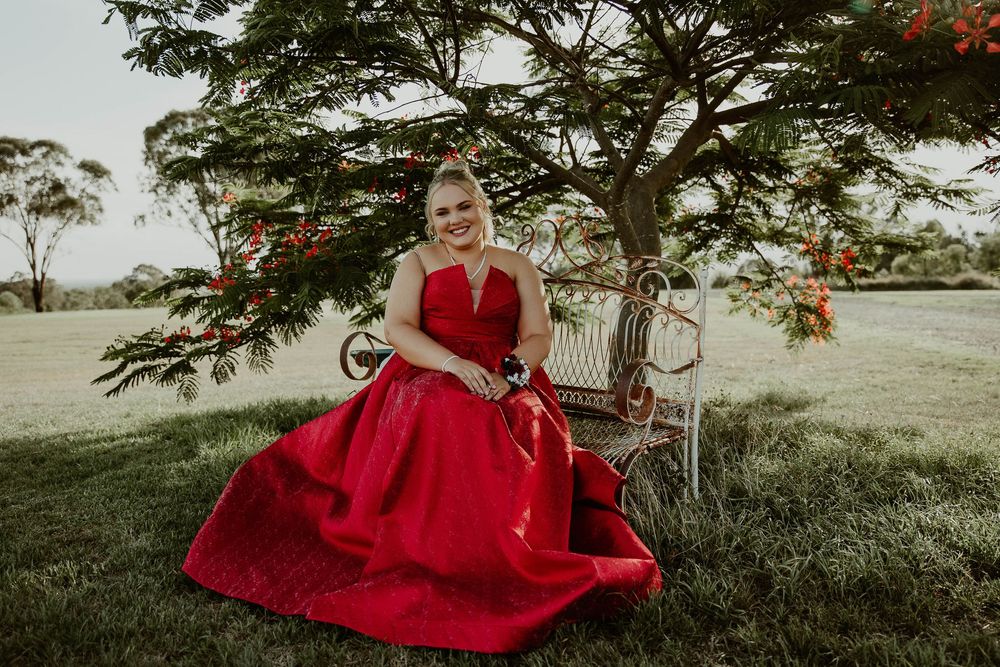 Graduate sitting on rustic chair under a tree at formal photo shoot