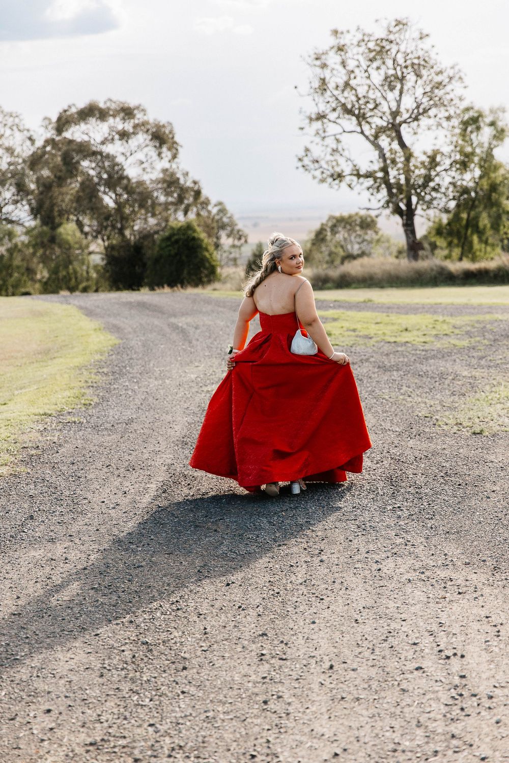 Graduate walking down the road looking over her shoulder at formal photo shoot
