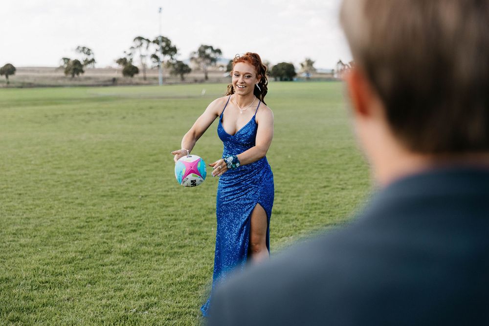 Graduate girl throwing a football to her partner at formal photo shoot
