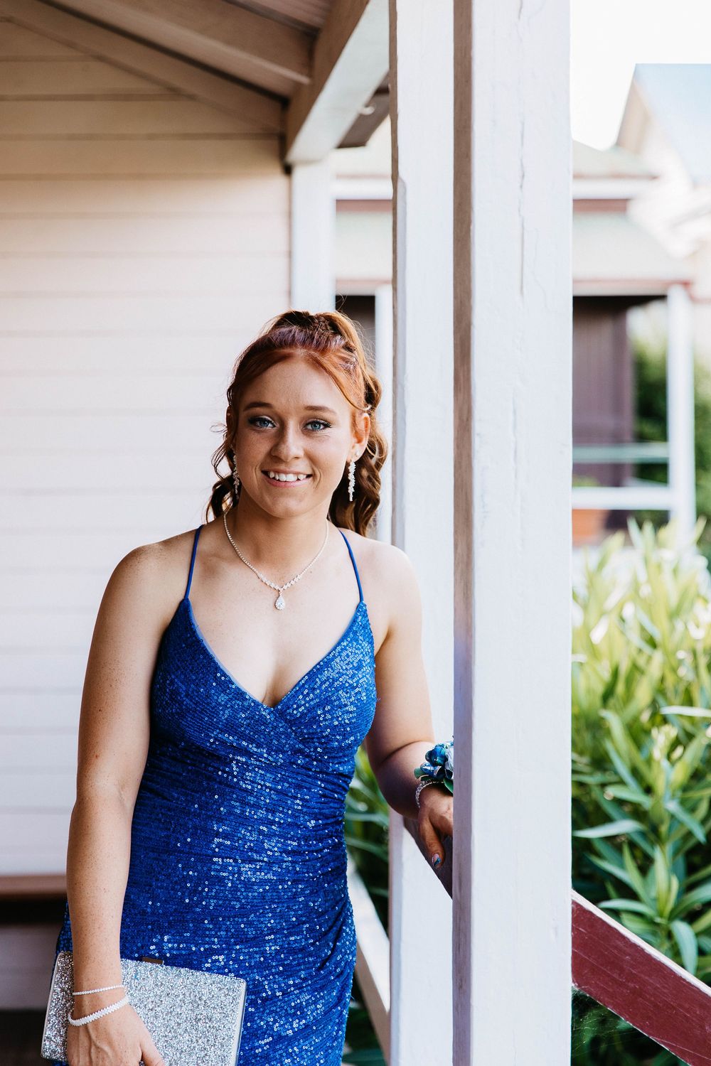 Graduate girl standing beside a pole on a verandah at formal photo shoot