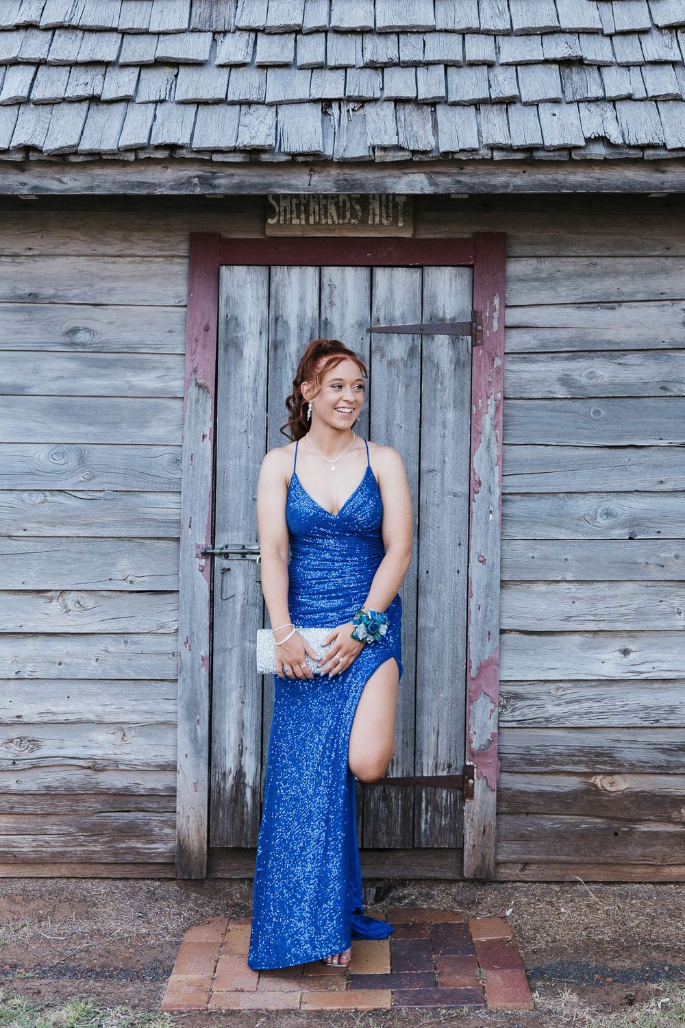 Graduate girl standing in front of wooden hut at formal photo shoot