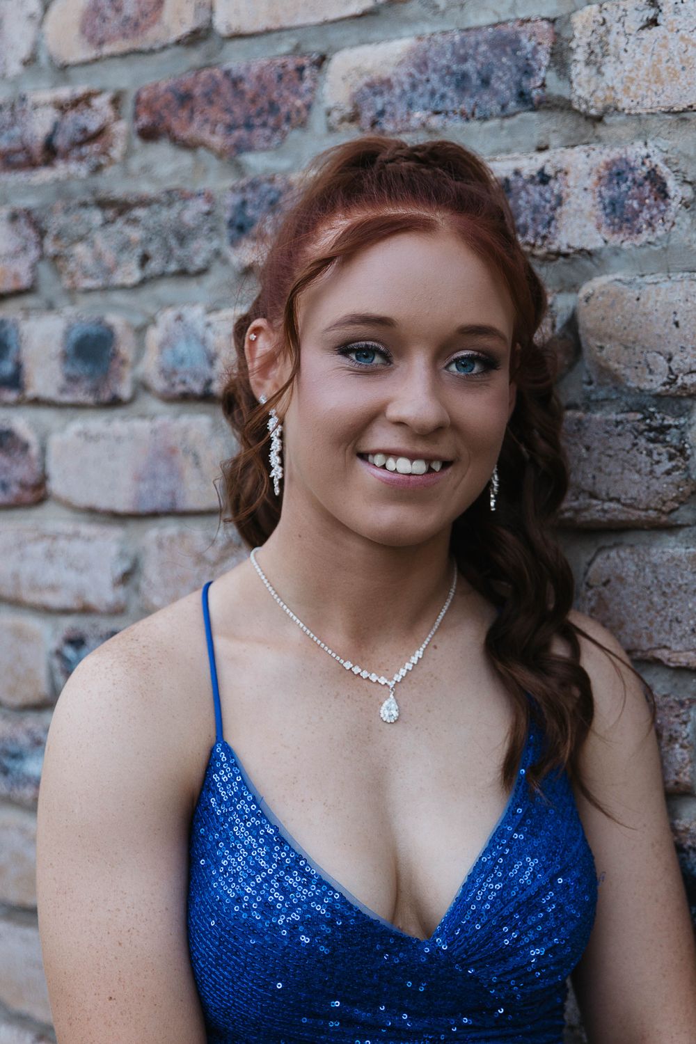 Graduate girl standing in front of brick wall at formal photo shoot