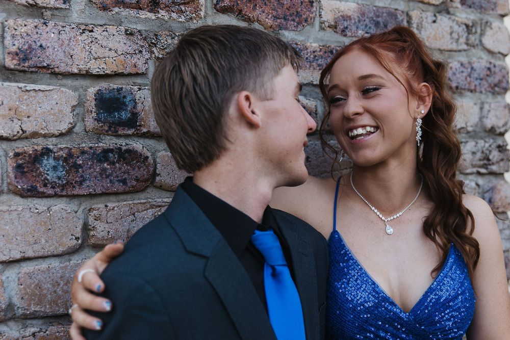 Couple standing in front of a brick wall laughing at formal photo shoot