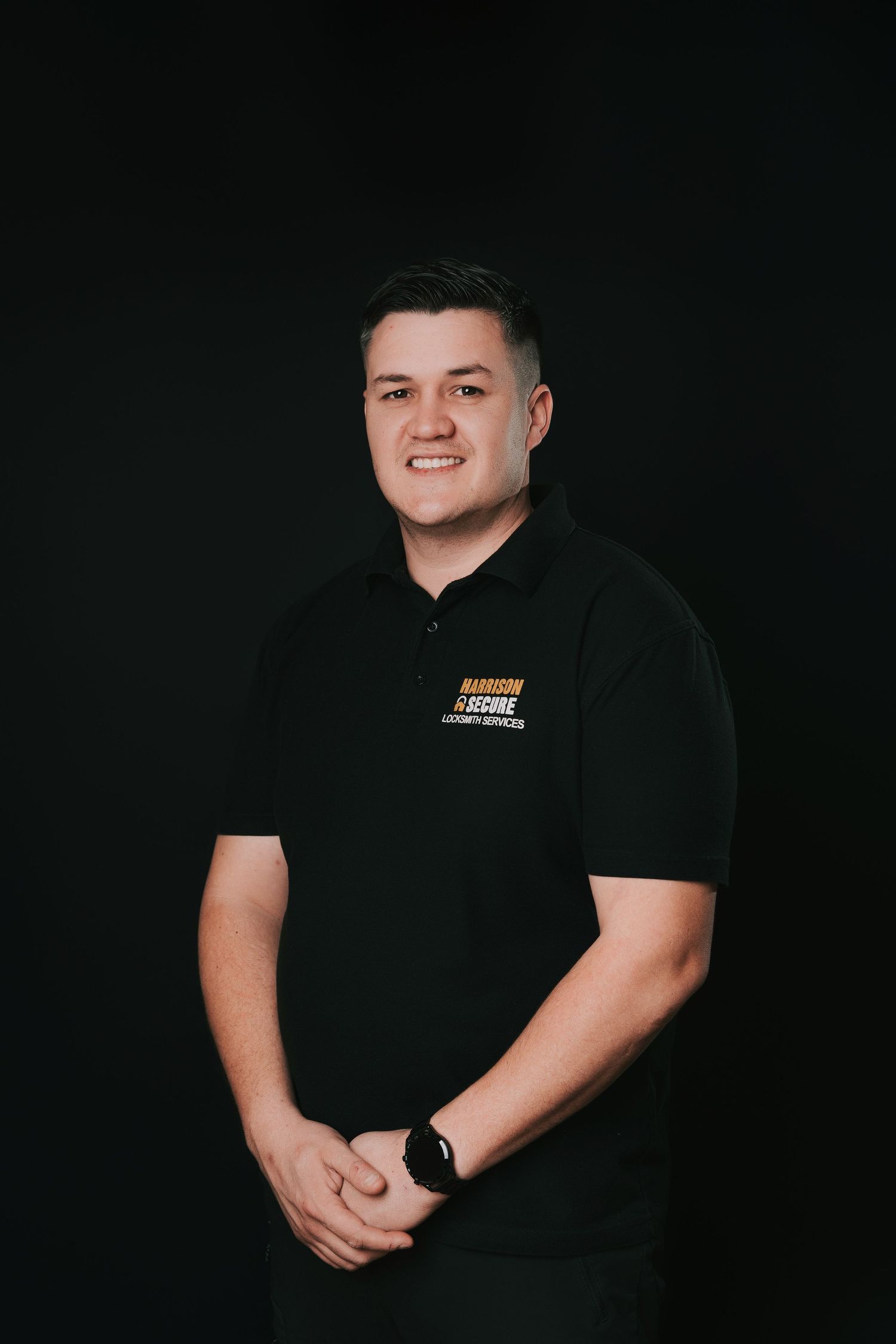 Professional studio portrait of someone wearing a black polo shirt with company logo against dark background.