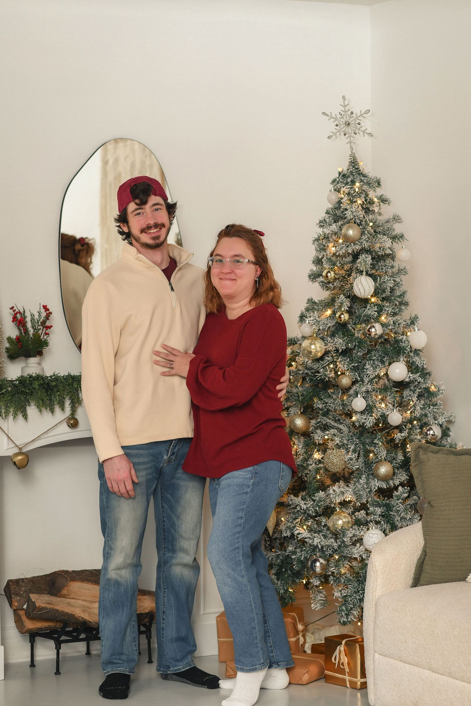 Couple posing by decorated Christmas tree in living room with festive decor.
