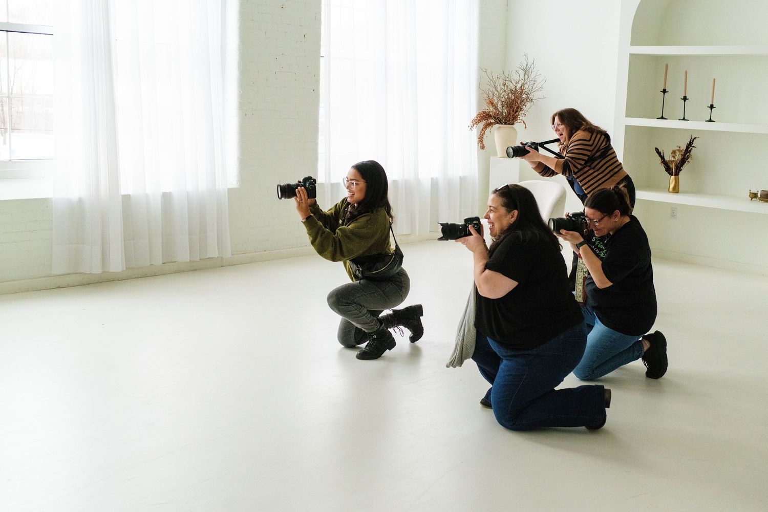 Three photographers crouching to capture shots in bright white studio space.