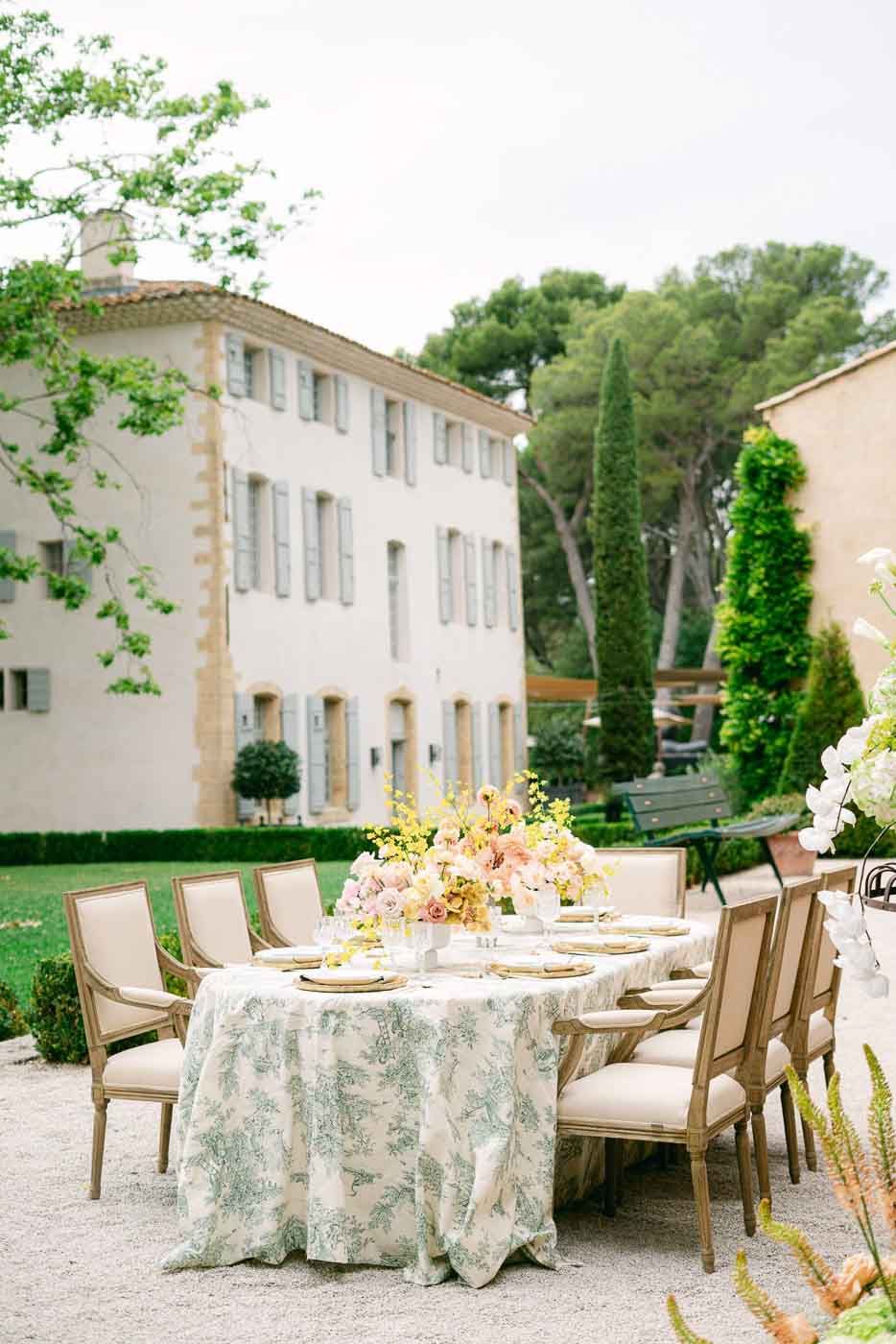 Table de réception en extérieur devant une bastide provençale, décoration florale et ambiance chaleureuse.