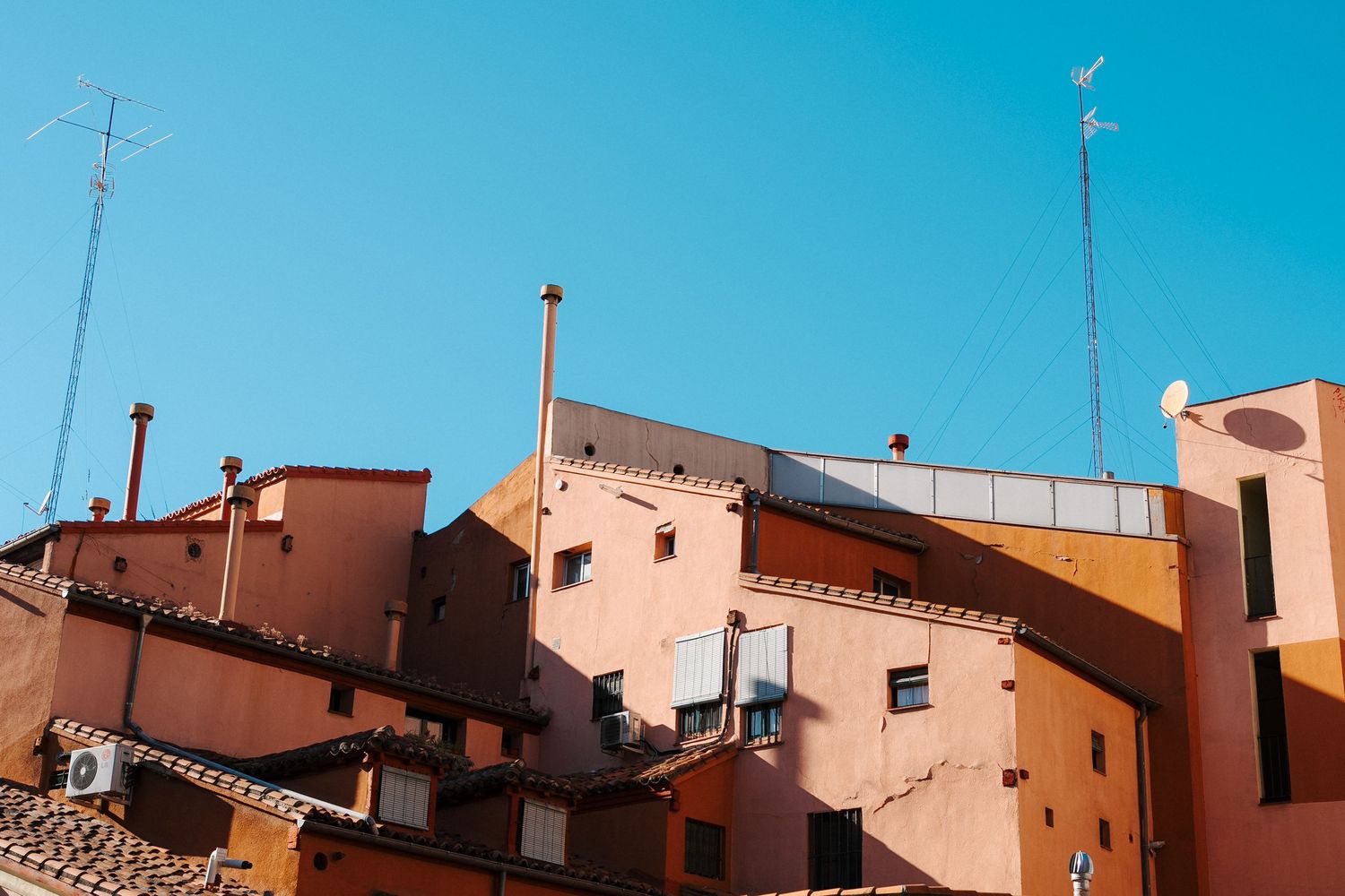 Geometric architectural details of terracotta buildings against bright blue sky with TV antennas on rooftops.