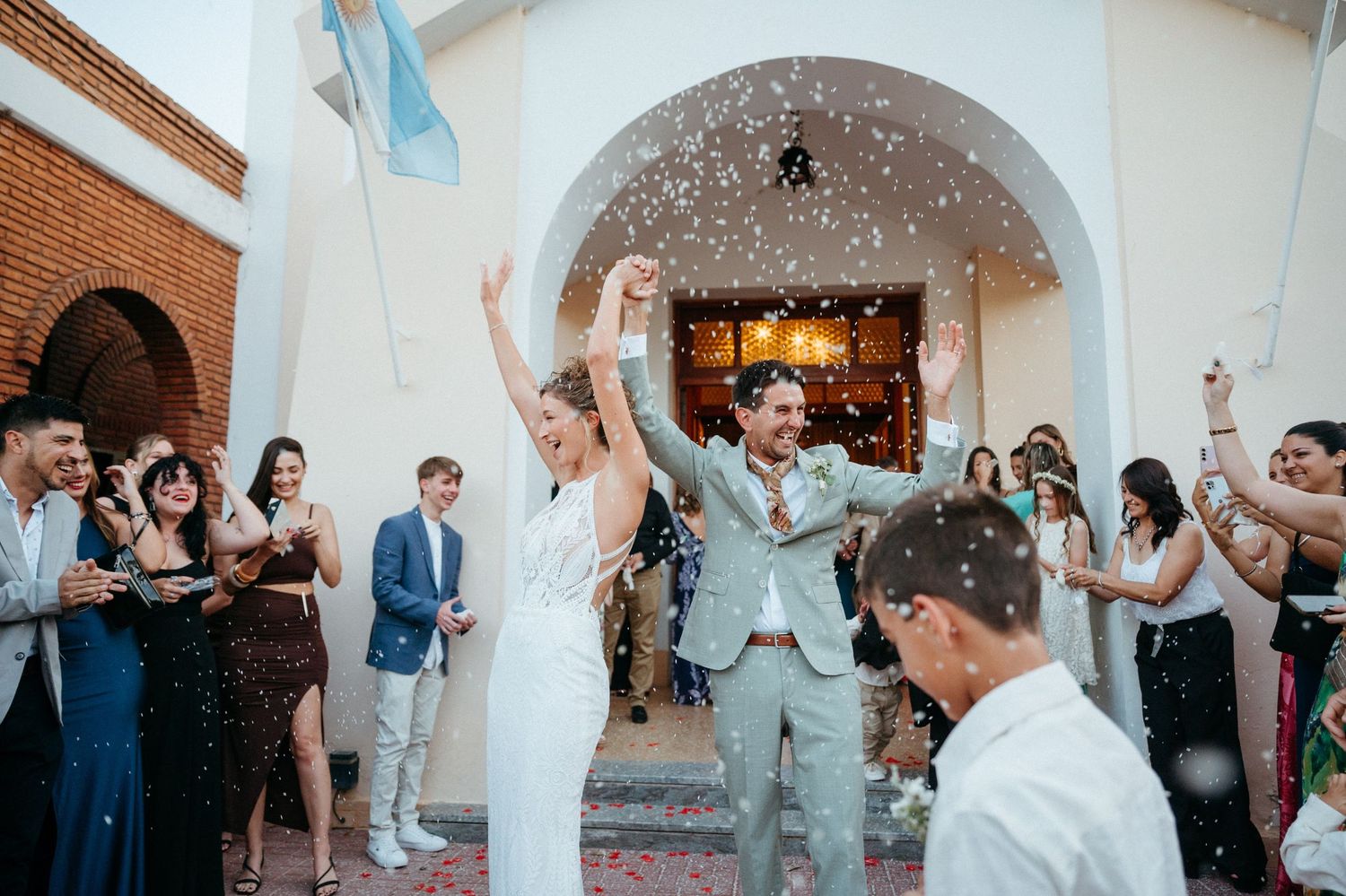 Wedding guests celebrate and dance together under white arched columns at an elegant reception venue.