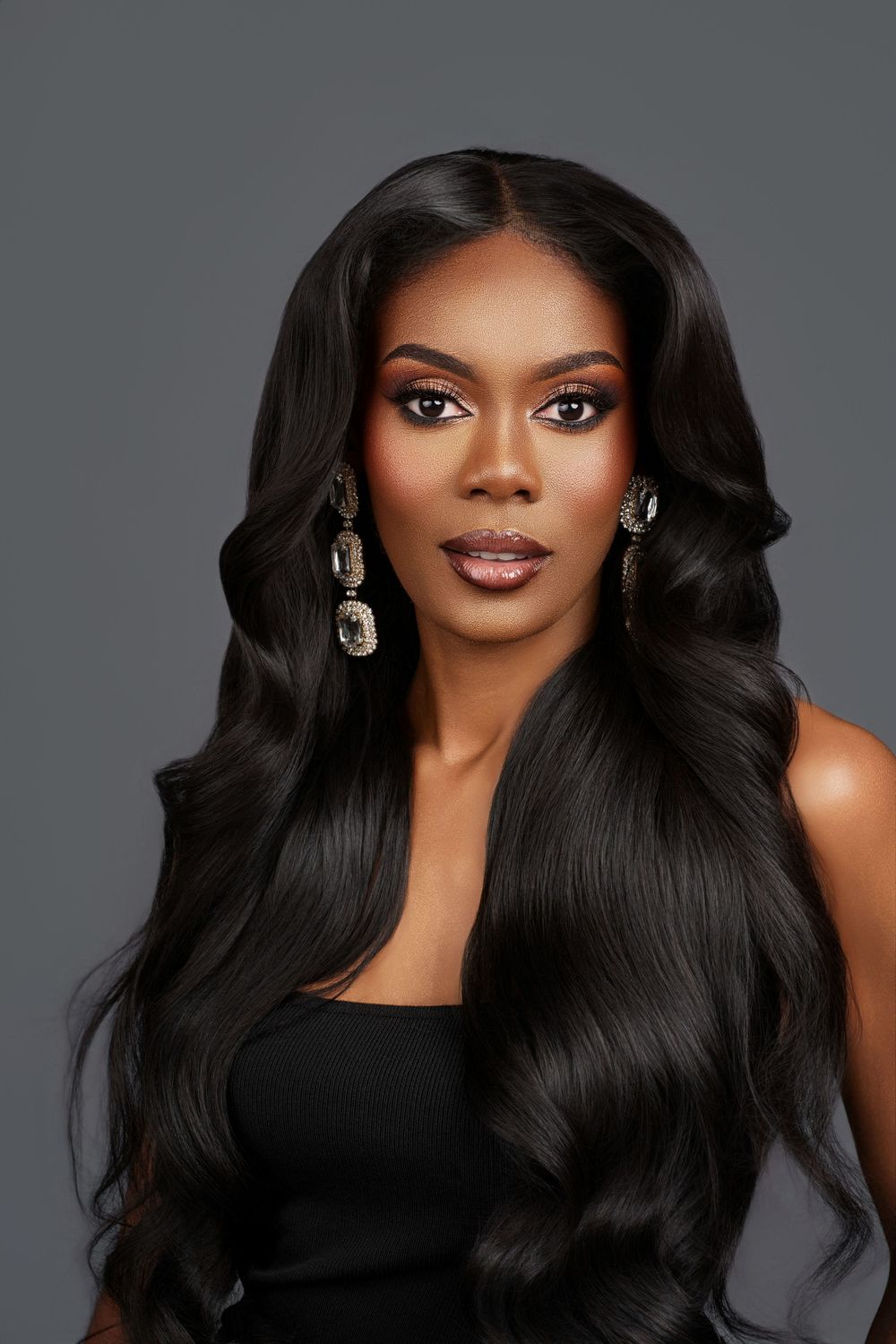 Professional beauty portrait with flowing black hair and glamorous makeup against dark gray background.