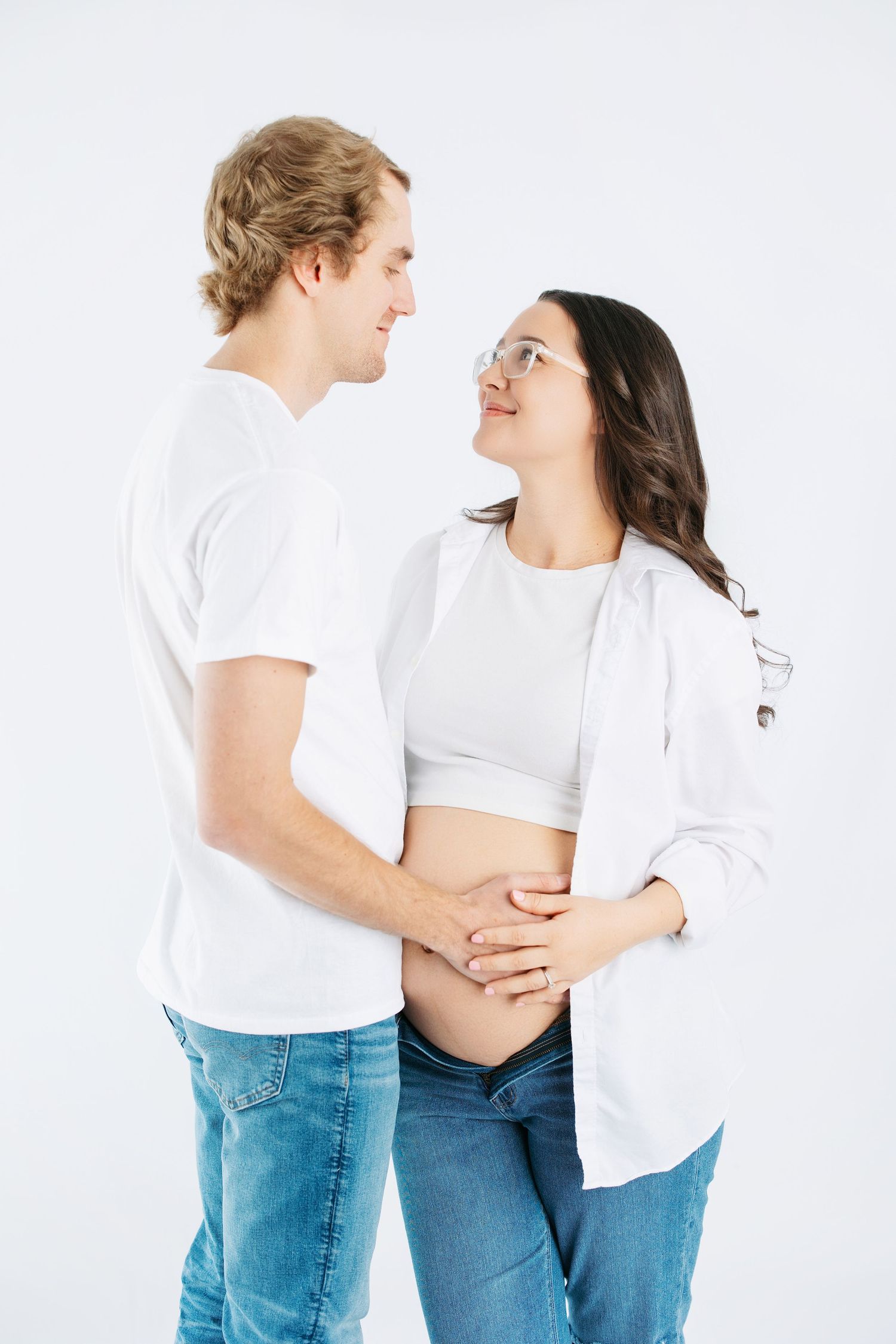 A couple in white shirts and blue jeans embraces while standing against a white background in a series of poses.