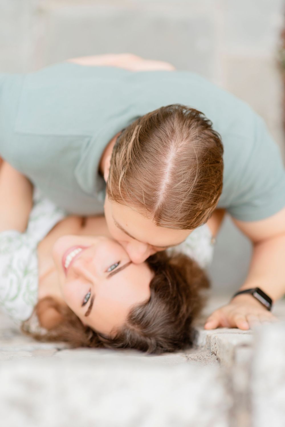 Romantic couple lying together on white bedding in soft morning light.