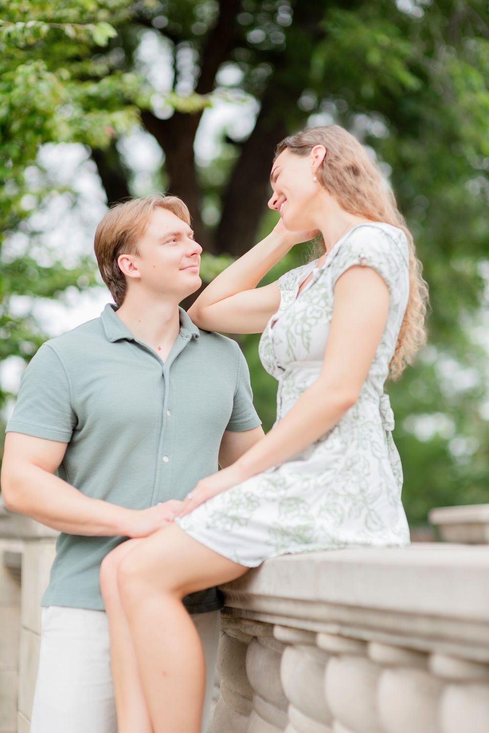 A couple shares an intimate moment against a stone balustrade in a garden setting.