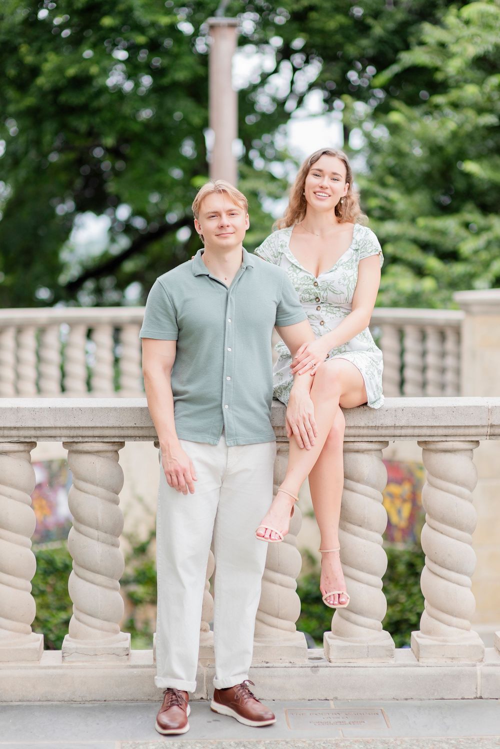 A couple poses together on ornate stone steps surrounded by lush greenery.