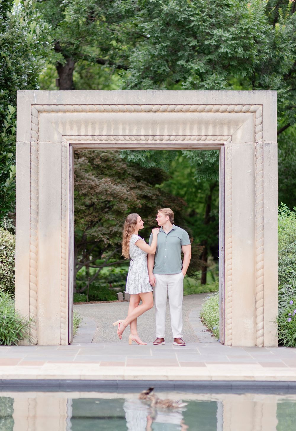 A couple shares a romantic moment under an ornate stone archway in a garden setting.