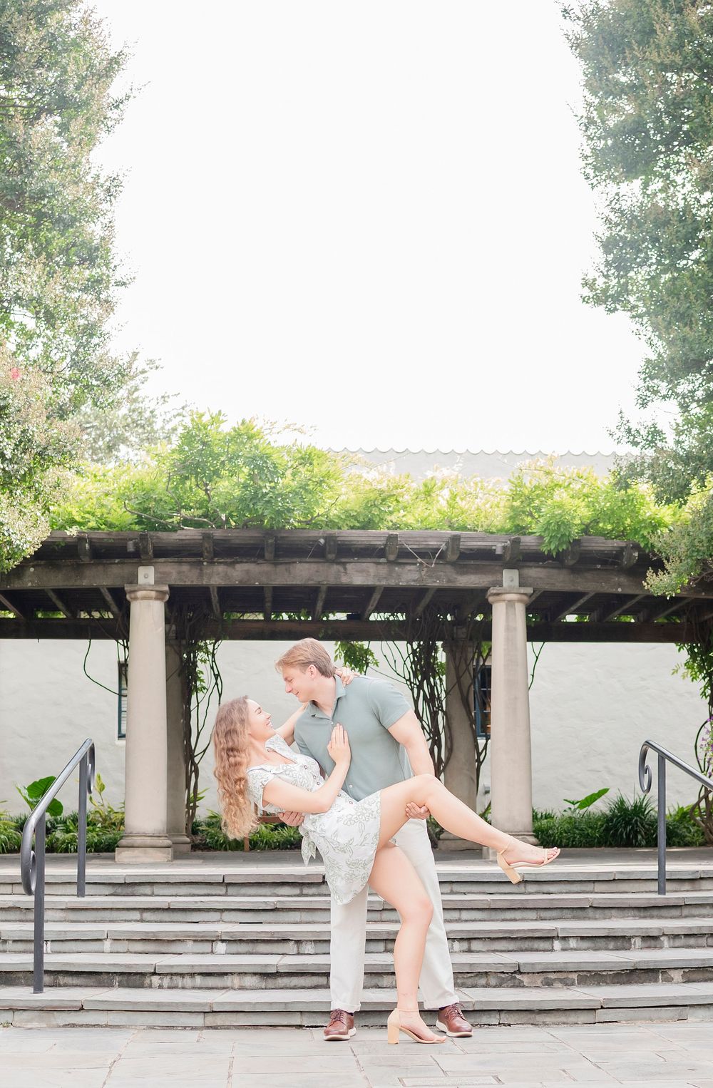 A romantic moment captured under a garden pergola with stone steps and lush greenery in the background.