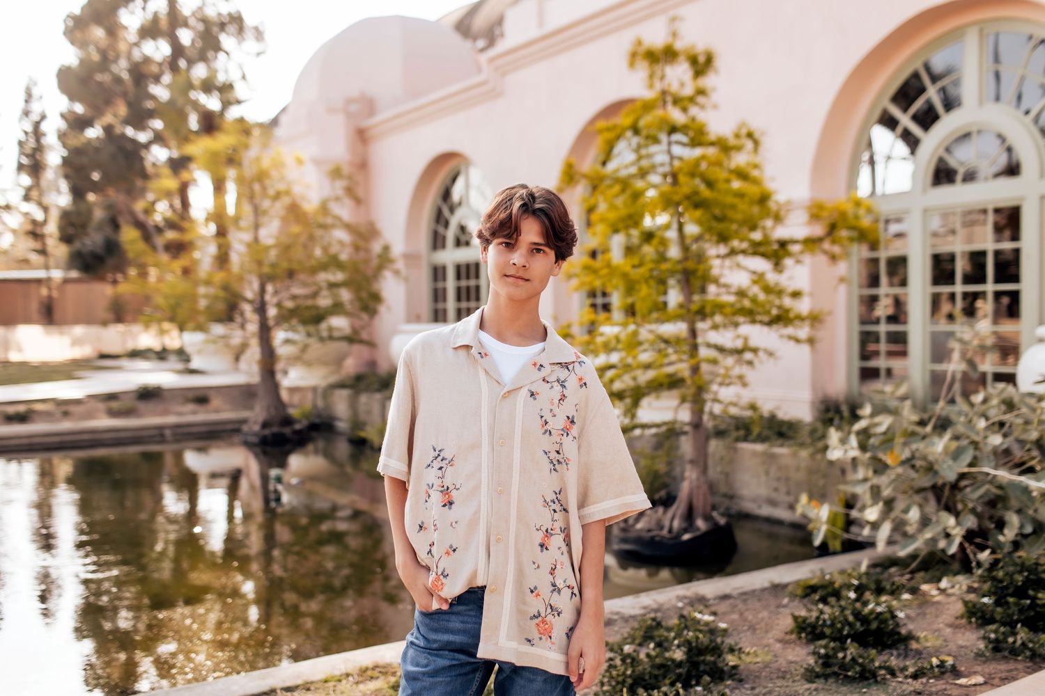 A senior boy stands confidently in front of the Balboa Park Botanical Garden in San Diego, CA.