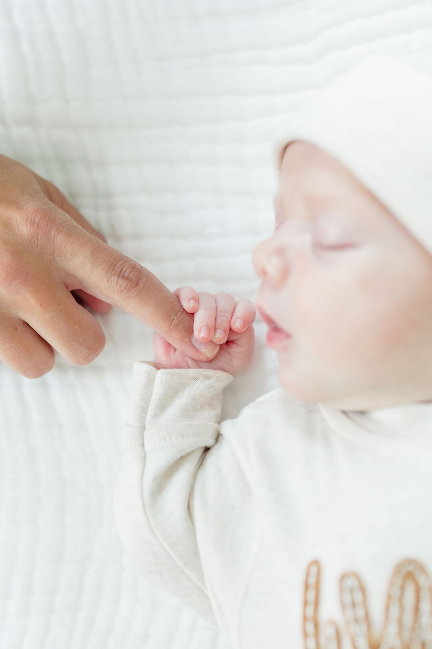 Close-up series of tender moments showing a baby's tiny hand grasping an adult's finger against white fabric.