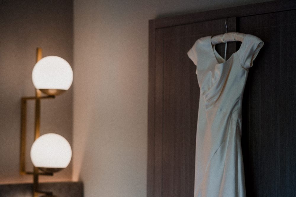 A light blue bridesmaid dress hangs elegantly against a dark wooden wall next to white globe light fixtures.